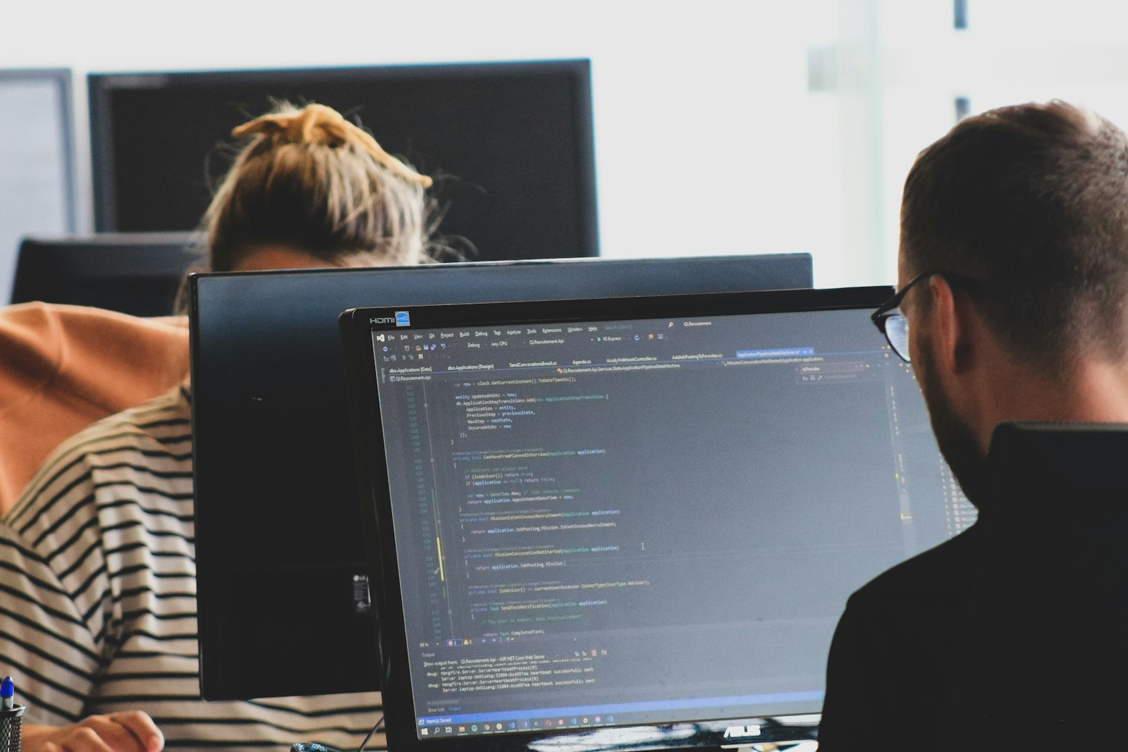 Two developers working on code at monitors in a bright open-plan office