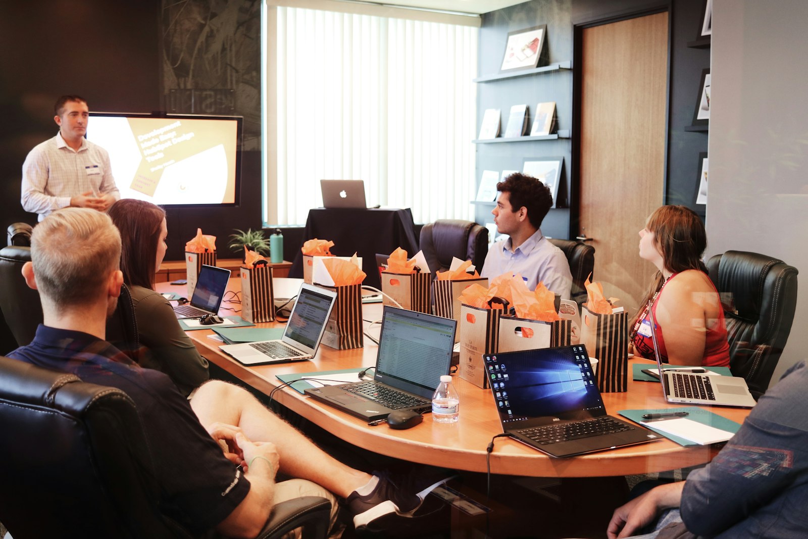 A team meeting around a boardroom table with laptops and a presentation screen