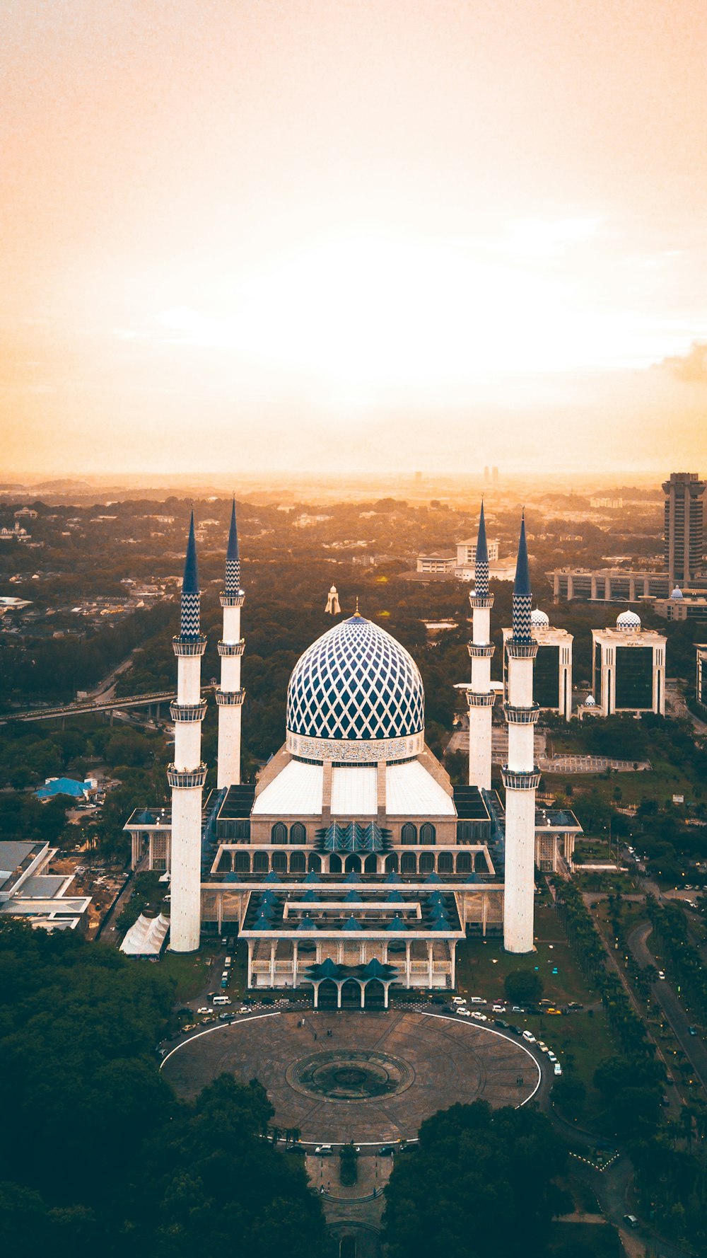 A white mosque with a patterned dome and four minarets at sunset